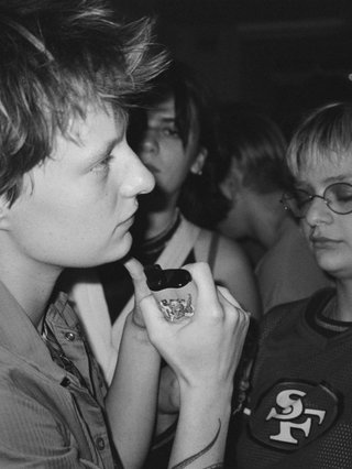 black and white flash photo of two people on dance floor. they are both looking out at the distance. person in front is holding a vape and there is a crowd behind them