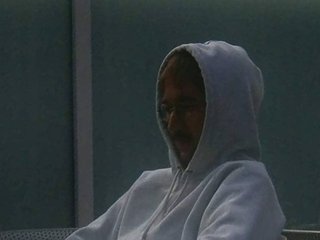 Lovefear sits in a chair with a grey hoodie on. He looks slightly sad as he stares at the floor.