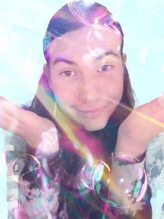 A picture of Jim making a cute shrugging gesture in front a baby blue background with tackily edited overlays of bubbles and lens flare.
