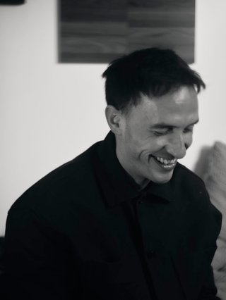 Ally McMahon of MidGround wearing a black jacket and collared shirt, smiling gleefully towards the right. Photograph is in black and white.