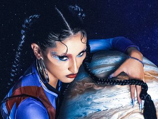 The image shows the artist JUPiTA in space looking down while clutching the planet Jupiter in her arms protectively.