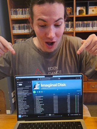 Jim excitedly pointing at their laptop which is showing their Album of the Week, Magdalena Bay's Imaginal Disk.