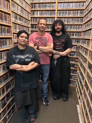Shareeka, Tomym and writer Omar El Akkad stand together in the fbi music library with their arms folded. They are coincidentally all wearing t-shirts with resistance artwork on them.