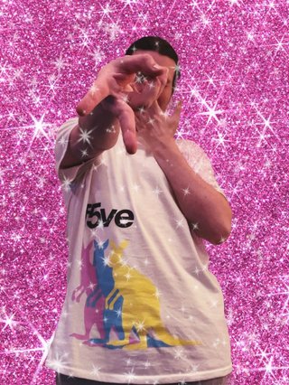 Jim wearing a f5ve tour t-shirt in front of a sparkly pink background. They are covering their face with one hand and have the other one extended in a peace sign towards the camera.