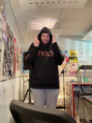 Jim standing in the fbi studio with a hood on, holding up two peace signs.