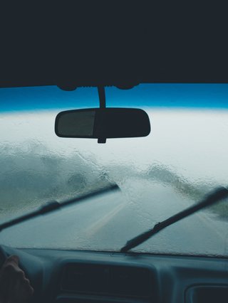 Interior shot of a car with the windshield wipers going.