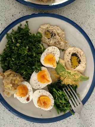 a breakfast plate featuring hummus, greens, pickles, nigela seeds and 4 egg halves
