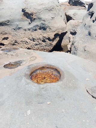 a small hole in a large rock filled with water. other large rocks in the background