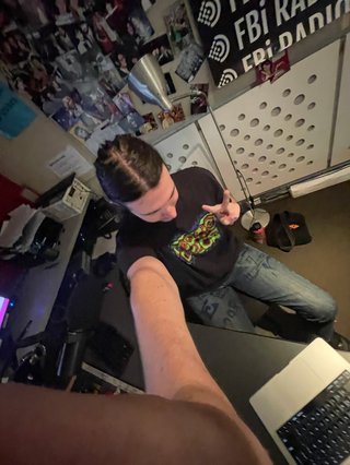 A 0.5x selfie taken from above of Jim in the studio holding up a peace sign.