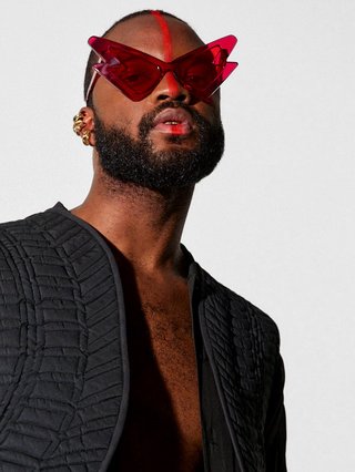 Genesis wears funky red sunglasses and a lowcut black jacket