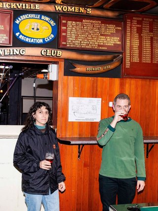A flash photo of a woman and a man standing candidly in a pub. They are both holding drinks.