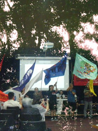A photo pf an Anakbayan action with flags of resistance in a crowd. The landscape of the philippines is overlayed in a minimal, inverted colours style