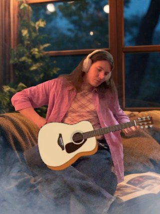 Jim sitting in a humble pose, they have been edited to be holding a guitar while sitting in a cozy lounge scene.