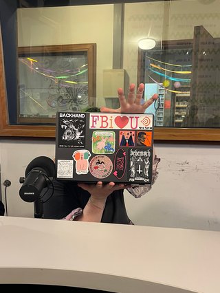 Charlie is holding up thier laptop to the camera, the laptop is covered in stickers.