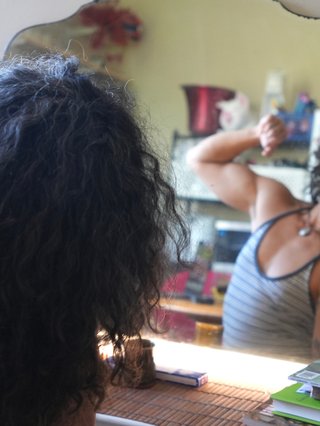 EJ flexes in the mirror, you can see their crowded shelf behind their reflection and they lean playfully to one side.