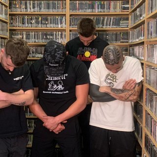 The two members of 700 Feel stand in the fbi music library with presenter John Troughton and artist Archie Mike. All four of them have their heads bowed.