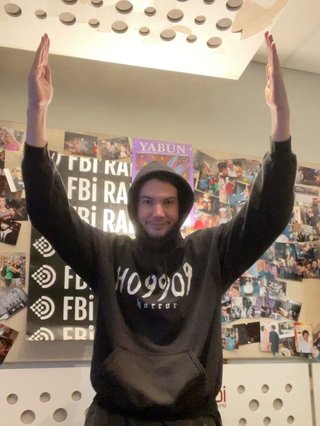 Jim in the fbi studio, making a U shape with their arms.