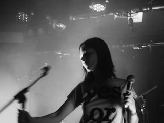 A black and white photo of Fatshaudi on stage. She is holding a microphone in one hand and a mic stand in the other.