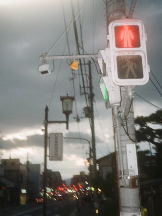 A film photograph of a street pole with a pedestrian crossing sign on it. It is sunset, and the clouds are silver and grey.