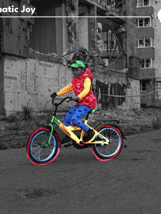 A young boy rides his bike in colour on a black and white background of a run down multi-story buildings.