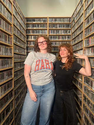 Kate, wearing a grey t-shirt, and Emma, wearing a black T-shirt, pose in the music library.