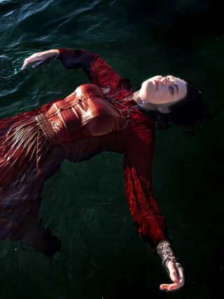 Amy Thing floats in dark ocean water. They're in a maroon dress body looking into the sky