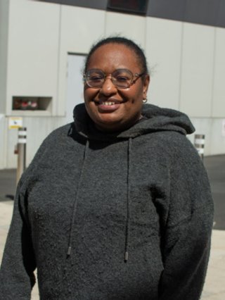 Anne smiles to camera, wearing glasses and a grey hoodie.