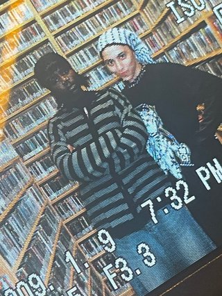 Attu and Sara standing in the fbi music library. They are both wearing monochrome and Sara wears a keffiyah. They stare strongly into the camera.