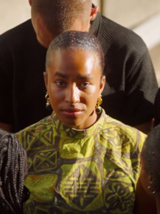 A still from a film with Binta Yade. She's looking strong and poised in the middle of the camera and she's surrounded by other young people in all black