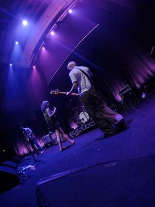 A photo of the three members of GAUCI performing live on stage at City Recital Hall, lit up by purple light.