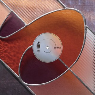 A maroon and red stained glass image with multiple panels. In the centre sits a CD