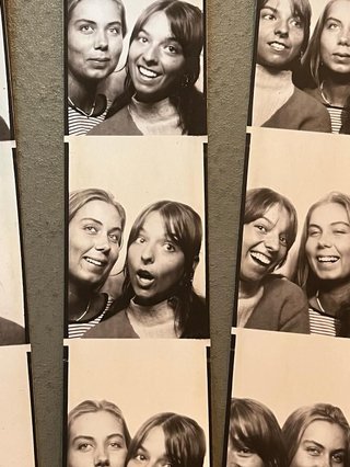 photo of two black and white film strip photo booth photos side by side. photo booth photos are of izzy and friend smiling and laughing next to each other