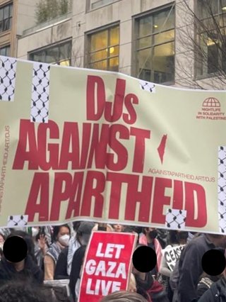 A banner in a protest crowd that reads in red: DJS AGAINST APARTHEID. A smaller red placard reads LET GAZA LIVE