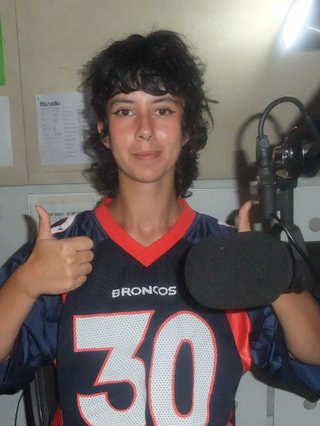 Ella Avne is in the studio giving two thumbs up in front of the microphone.