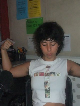 Ella Avne is in the studio posing with their arm muscles flexed.
