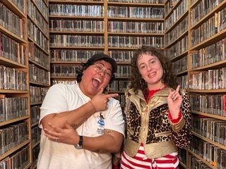Diana and Freddy posing in the music library. Diana is pointing at Freddy, who is posing with a peace sign