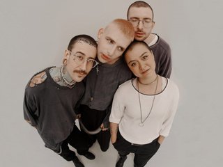 The four members of Hydra Fashion Week photographed from a high angle in a fish-eye style, huddled together on a white photo studio background