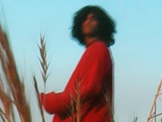 Moody stylised portrait of artist 'To Oscar' standing in a field with dusk blue sky in the background, wearing a red jumper.