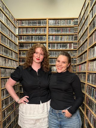 Two women standing next to each other smiling in a CD library