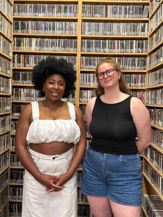 Chika and Kate stand in the music library and smile to camera.