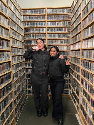 Naz and Tanya pose standing and smiling in the music library, surrounded by CDs.