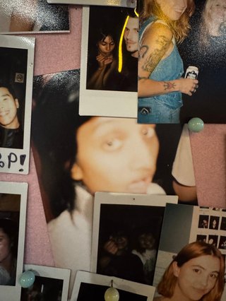 A picture of a pinboard of printed pictures. There is a blurry, candid picture of Maleeka in the centre.