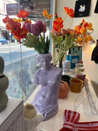a purple vase in the shape of a statue with tulips that are orange, pink and purple coming out the top.