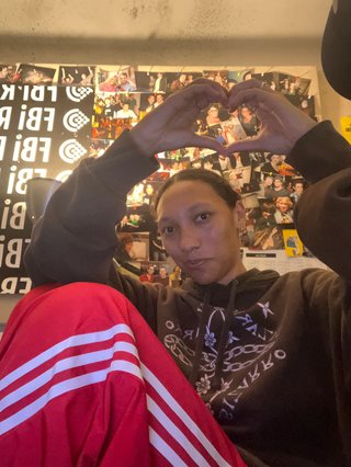 Bri wearing red pants and a grey jumper with her hands in the shape of a heart