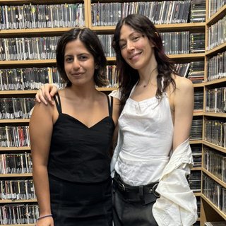 Tanya Ali and Caroline Polachek stand in the fbi.radio cd library. They are smiling and looking at the camera. Caroline has her arm over Tanya's shoulder.