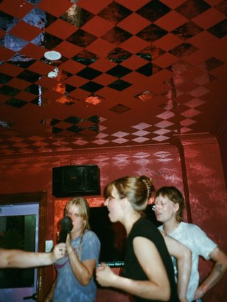 izzy is in a red karaoke room with two others behind her and a microphone held up to her