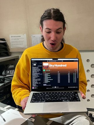 Jim with an impressed look on their face, holding up their laptop which is showing the album Sky Hundred by Parannoul.