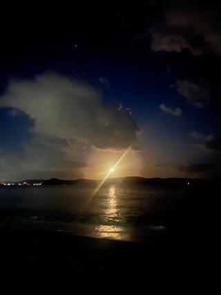 An image of a hazy full moon low over the horizon over the ocean in the cloudy night sky