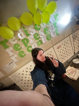 A 0.5x selfie of Jim in the studio in front of the sign showing the theme for this year's Supporter Drive: rediscover, represent, reconnect.