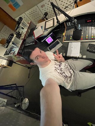 A 0.5x selfie of Jim in the fbi radio studio holding up a peace sign and pouting at the camera.